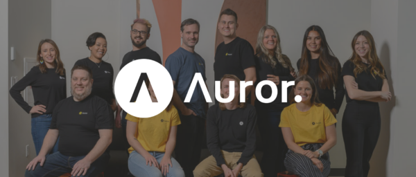 team photo of diverse individuals wearing branded shirts in an office setting, Auror team group photo with logo and branding