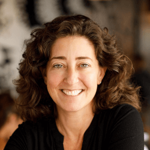 smiling woman with curly hair in a casual black top, bright background creating an inviting atmosphere