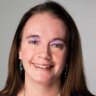 headshot of a smiling woman with long brown hair, purple eyeshadow, and dangling earrings, professional portrait in soft lighting
