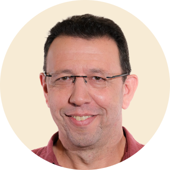 smiling man with glasses in a circular frame, casual portrait with neutral background and warm expression