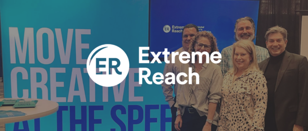 Extreme Reach team at event, showcasing branding with blue backdrop and creative slogan on display. Team smiles together. Extreme Reach, Team Event
