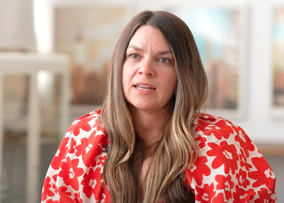 woman with long brown hair in a red floral top, engaged in conversation, background features soft home decor, engaged conversation, vibrant floral attire, soft-focus background