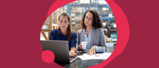 business women collaborating, analyzing data on laptop with documents in a warehouse setting