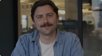 man with a mustache in a light blue denim jacket, modern office setting with blurred background elements