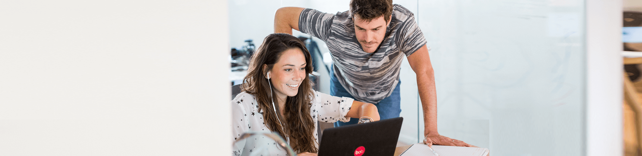 working professionals collaborating, woman smiling at laptop with man assisting in a modern office environment