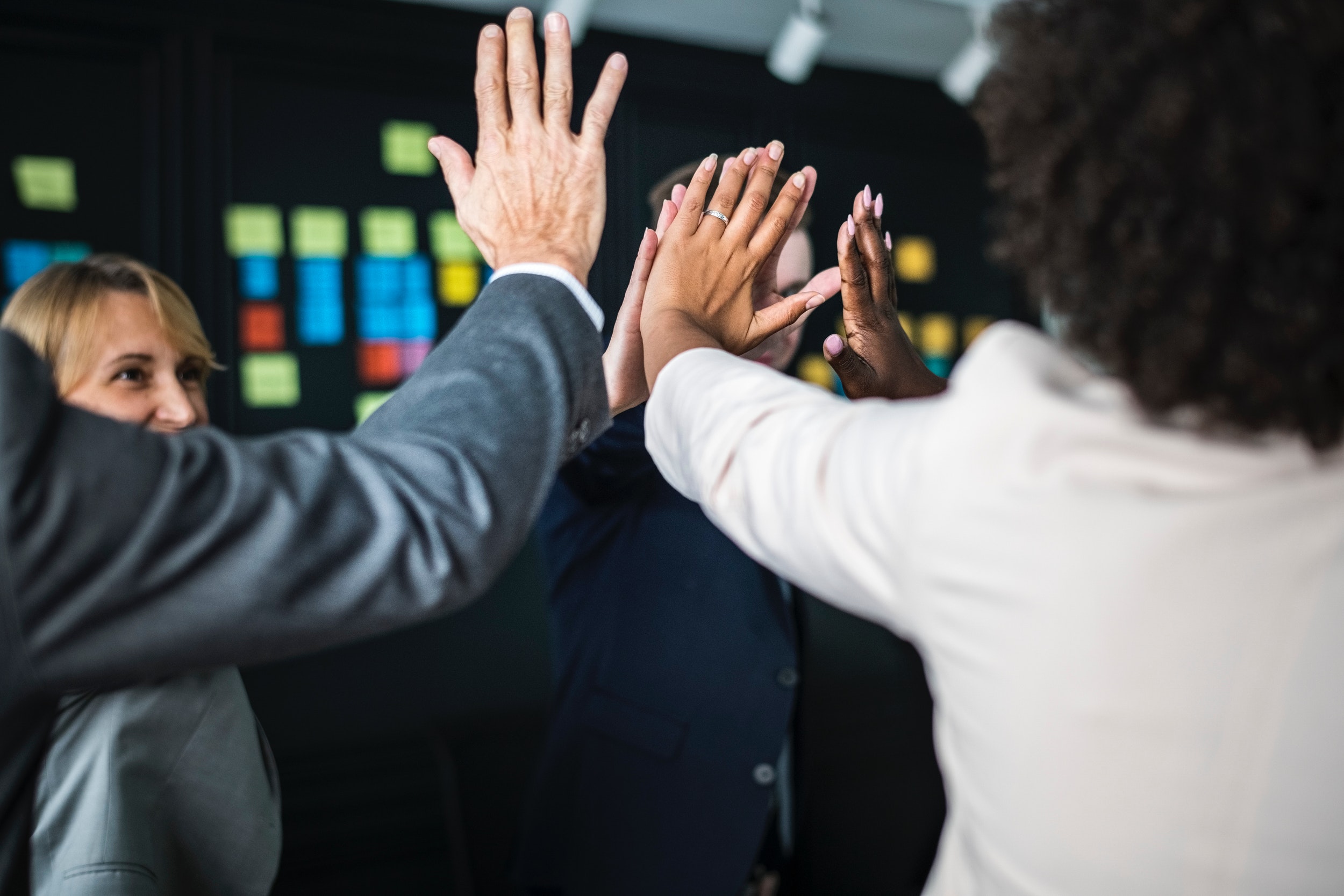 team collaboration, hands raised in celebration against a backdrop of vibrant sticky notes