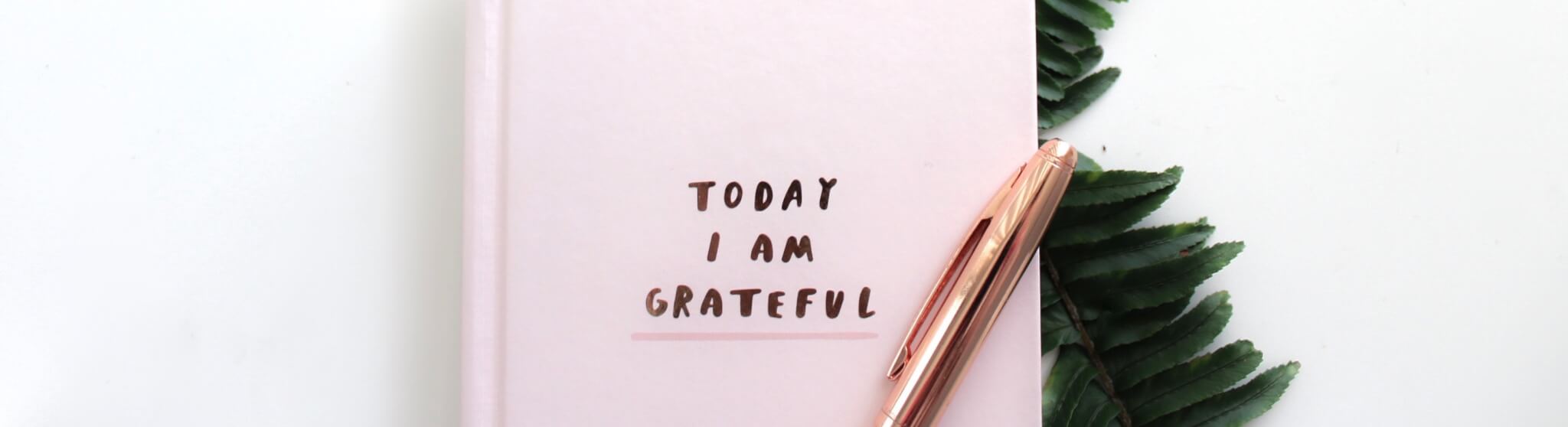 journal with "Today I Am Grateful" text and a rose gold pen beside green leaves, grateful journal with elegant design and pen